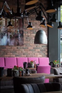 Stilvoll eingerichteter Sitzbereich mit pinker Polsterbank und rustikaler Backsteinwand im Loft’s Steakhaus Ingolstadt.